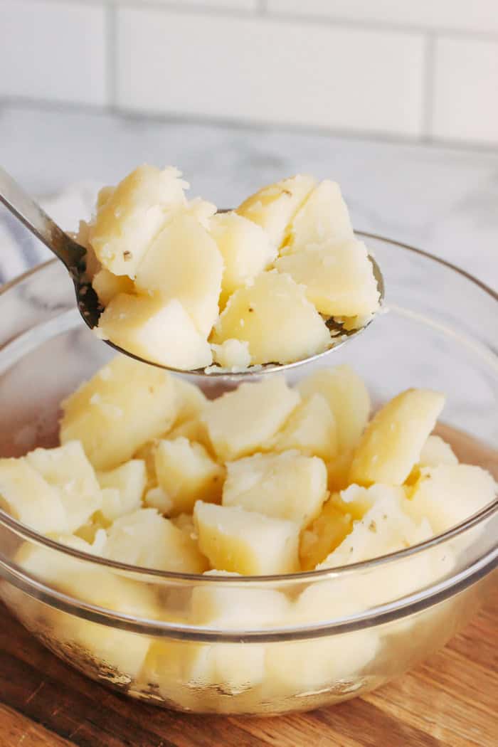 a spoon of cut, cooked potatoes over a clear bowl of potatoes