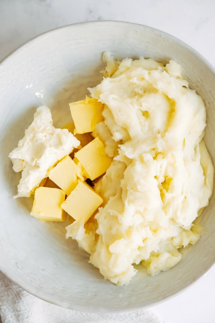a large bowl with mashed potatoes, cream cheese, and butter