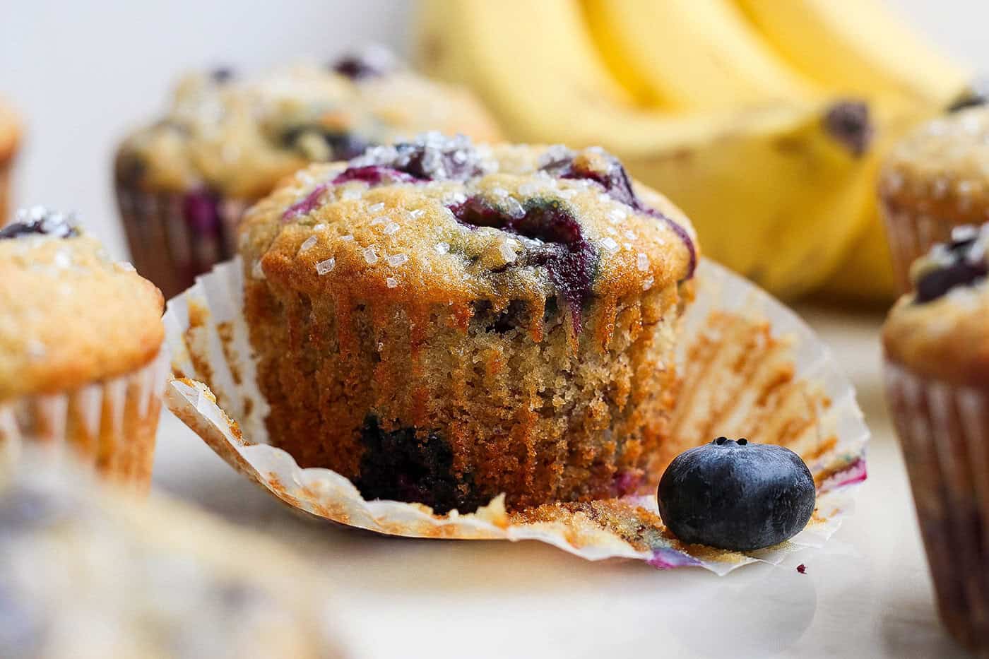 Banana Blueberry Muffins combine two classic recipes into one moist, lofty, perfectly sweet muffin package. They're such a treat! Closeup of banana blueberry muffin with wrapper pulled off
