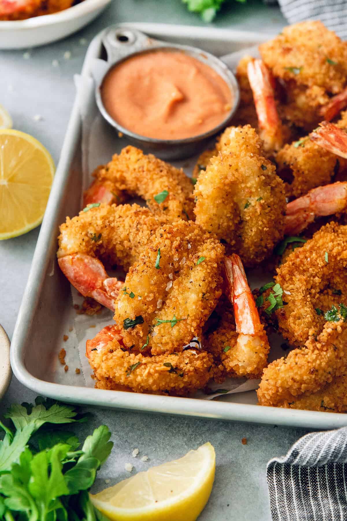 These butterfly shrimp are tender and juicy on the inside, crisp and crunchy on the outside, and paired with a spicy creamy cocktail sauce! Crispy butterfly shrimp on metal tray with creamy cocktail sauce