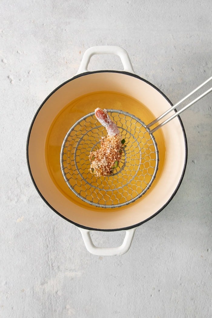 These butterfly shrimp are tender and juicy on the inside, crisp and crunchy on the outside, and paired with a spicy creamy cocktail sauce! Overhead view of shrimp being dropped into pot of oil