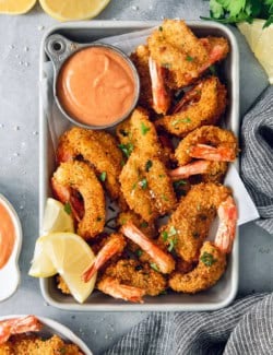 Crispy butterfly shrimp in metal tray with cocktail sauce and lemon wedges