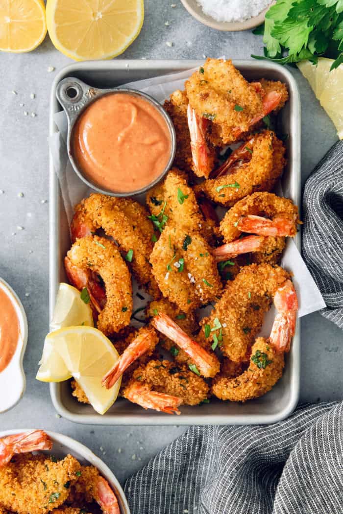 These butterfly shrimp are tender and juicy on the inside, crisp and crunchy on the outside, and paired with a spicy creamy cocktail sauce! Crispy butterfly shrimp in metal tray with cocktail sauce and lemon wedges