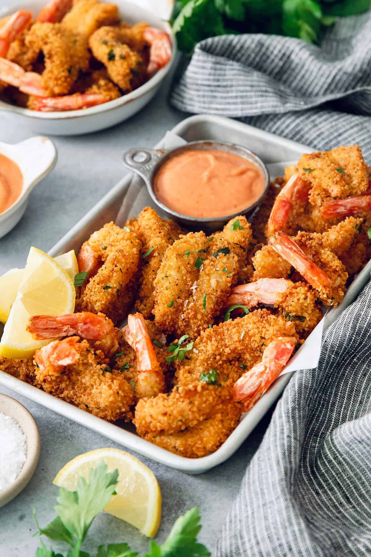 These butterfly shrimp are tender and juicy on the inside, crisp and crunchy on the outside, and paired with a spicy creamy cocktail sauce! Butterfly shrimp in tray with cocktail sauce and lemon wedges