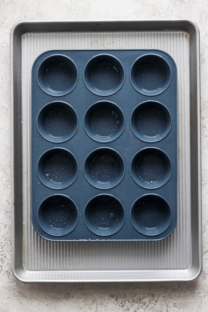 Cottage Cheese Egg Bites are creamy, cheesy and packed with protein. And let’s not forget the bacon! The perfect savory meal prep breakfast. Overhead view of silicone muffin pan coated with oil