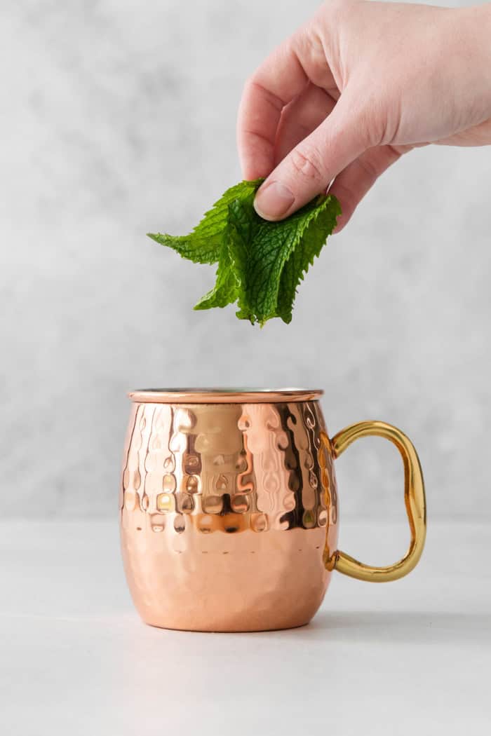 This easy Moscow Mule Mocktail has the bold ginger, tart lime and refreshing mint flavor you love, minus the alcohol. Perfect for summer! Hand placing mint leaves in copper mug