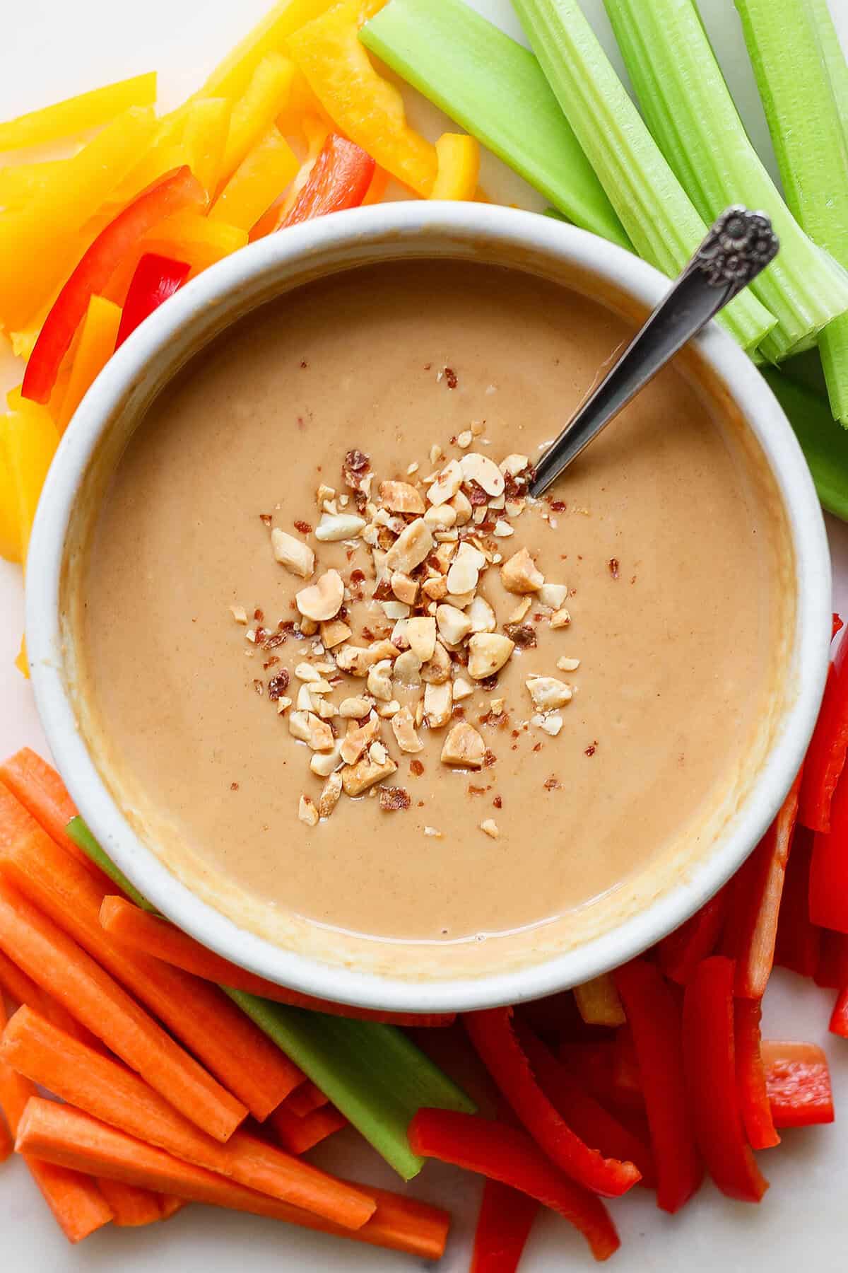 This homemade peanut sauce is creamy and sweet, but also tangy, garlicky, and just a little bit spicy. But best of all, it's SO easy to make! Overhead view of peanut sauce in bowl with spoon, on platter of fresh vegetables for dipping