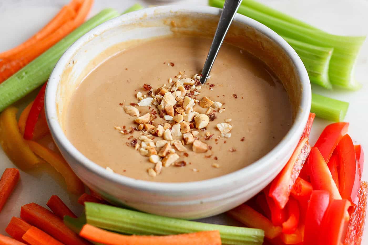 This homemade peanut sauce is creamy and sweet, but also tangy, garlicky, and just a little bit spicy. But best of all, it's SO easy to make! Bowl of peanut sauce topped with chopped peanuts, surrounded by crudite
