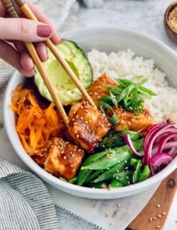 Chopsticks picking up teriyaki salmon bite from bowl