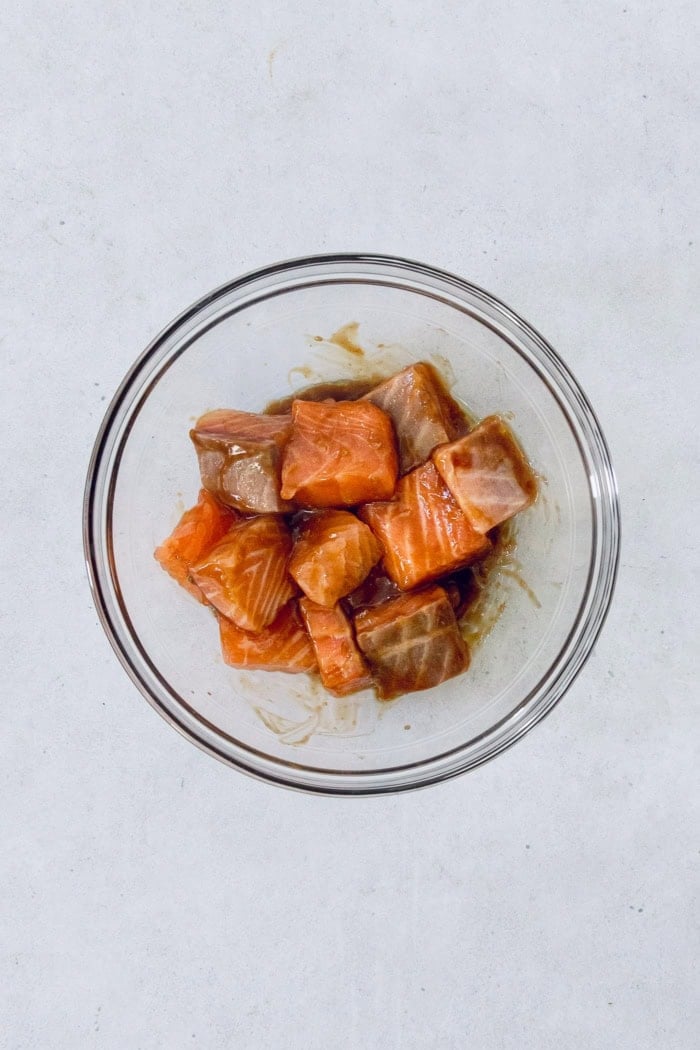 Teriyaki salmon bowls are an easy dinner ready in less than 20 minutes, with tender salmon, sticky teriyaki sauce, and lots of fresh veggies! Overhead view of raw salmon with oil and teriyaki sauce in bowl