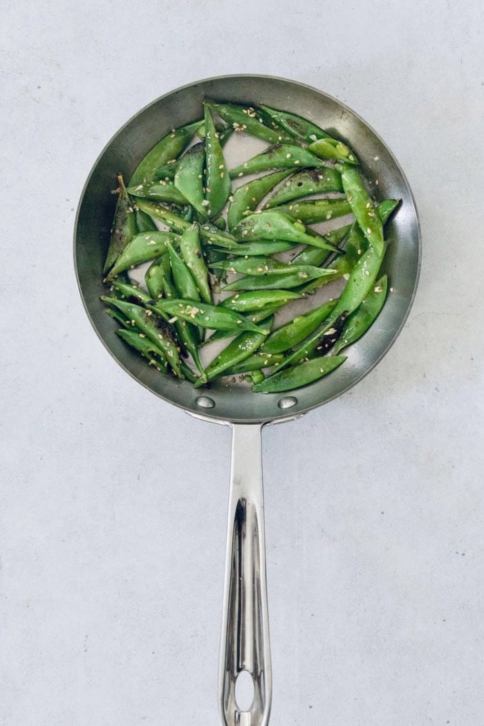 Teriyaki salmon bowls are an easy dinner ready in less than 20 minutes, with tender salmon, sticky teriyaki sauce, and lots of fresh veggies! Overhead view of snap peas cooking in skillet
