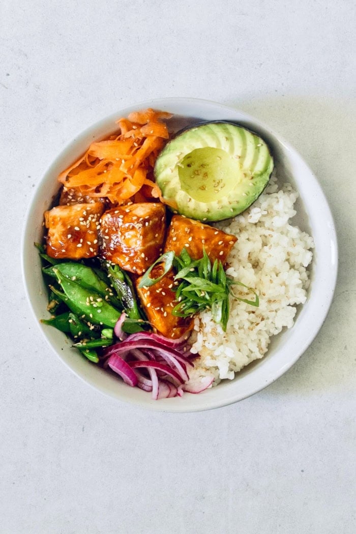 Teriyaki salmon bowls are an easy dinner ready in less than 20 minutes, with tender salmon, sticky teriyaki sauce, and lots of fresh veggies! Overhead view of teriyaki salmon bowl with avocado, carrots, snap peas, and rice
