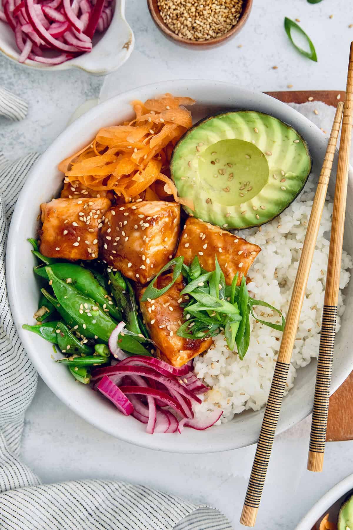 Teriyaki salmon bowls are an easy dinner ready in less than 20 minutes, with tender salmon, sticky teriyaki sauce, and lots of fresh veggies! Overhead view of teriyaki salmon bowl with avocado, carrots, snap peas, and rice