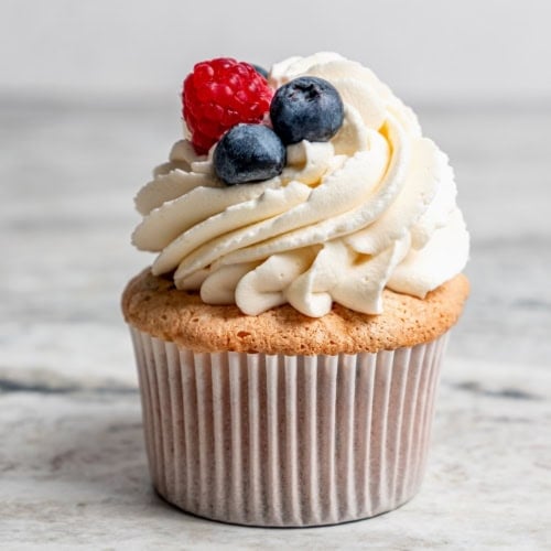 an angel food cupcake topped with white frosting and fresh berries