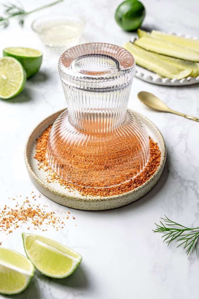 This Pickle Margarita recipe is bright and citrusy just like the classic, but it has a little extra pop of flavor to make it truly special! Dipping margarita glass in plate with Tajin