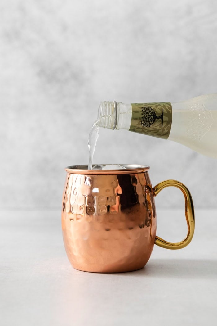 This classic Moscow mule recipe combines lime juice, ginger beer, and vodka with a sprig of fresh mint for a supremely refreshing cocktail! Pouring ginger beer into copper mug for Moscow mule