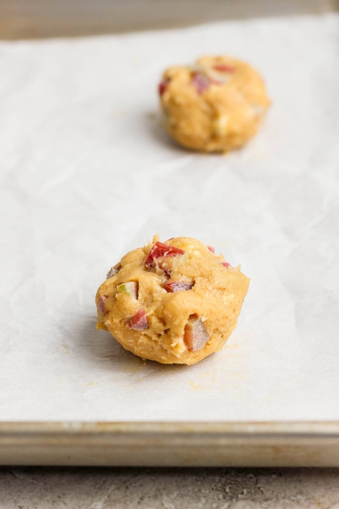 These easy Rhubarb Cookies are buttery, chewy, and a must-make for rhubarb season. White chocolate and flaky salt make them truly special! Balls of rhubarb cookie dough on parchment-lined baking sheet