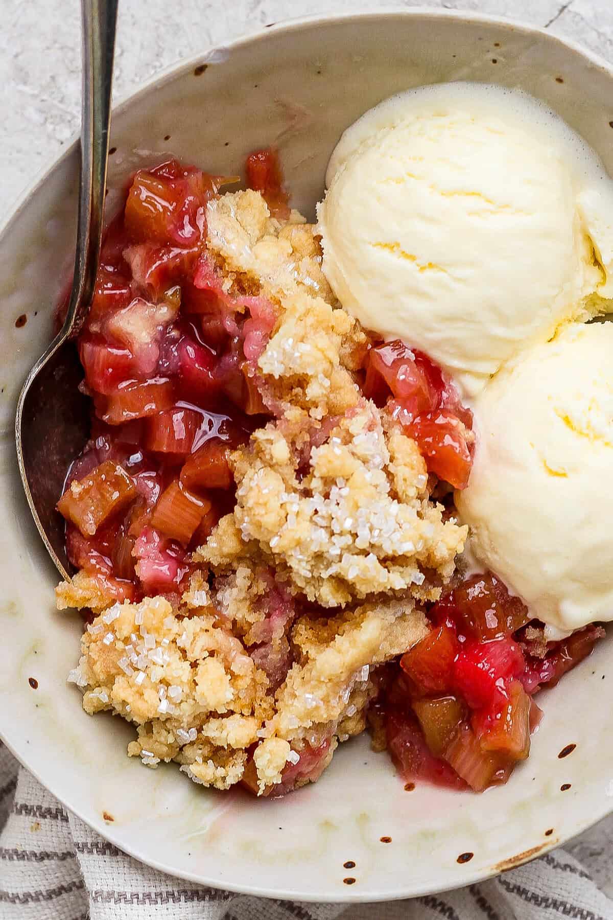 Overhead view of rhubarb dump cake in bowl with spoon and scoops of vanilla ice cream
