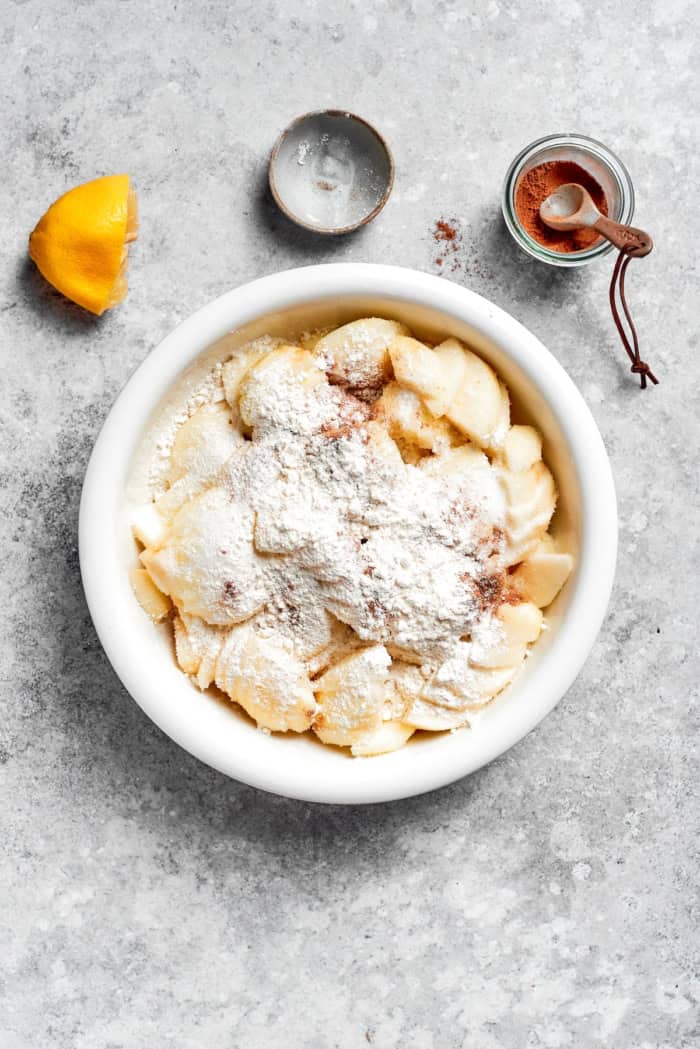 Apple Cobbler has apple pie flavor in an easier form, swapping the crust for a biscuit-like topping that bakes up tender and golden brown! Overhead view of flour and spices added to bowl of apples