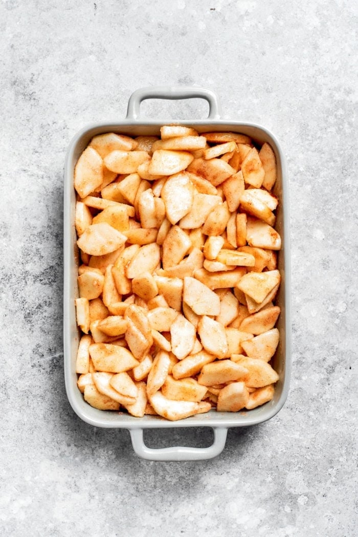 Apple Cobbler has apple pie flavor in an easier form, swapping the crust for a biscuit-like topping that bakes up tender and golden brown! Overhead view of spiced apples in baking dish