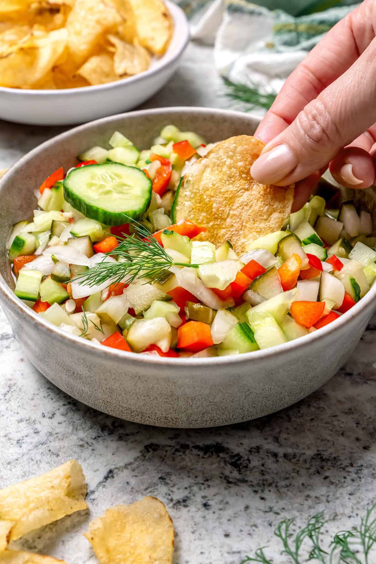 Inspired by Grillo's, this Pickle de Gallo recipe is oh so easy to make and packs in big, briny pickle flavor. Use it as a dip or condiment! Digging potato chip into bowl of pickle de gallo
