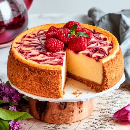 Raspberry cheesecake on a platter, with a piece removed