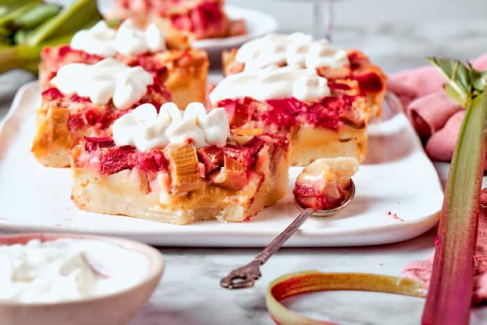 Buttery shortbread is layered with rhubarb custard to create these irresistible Rhubarb Custard Bars. Don't skip the cream cheese topping! Rhubarb custard bars on platter with spoon