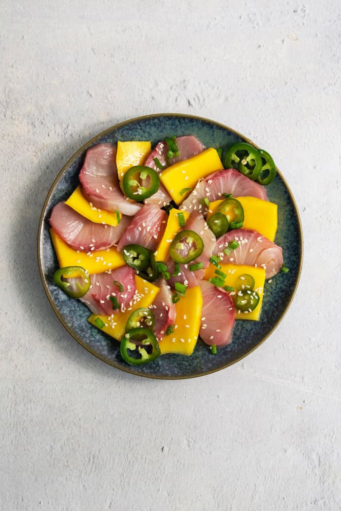 Sweet mangoes and pickled jalapeño peppers make this Hamachi Crudo recipe a standout! It's an easy appetizer that always impresses. Overhead view of hamachi crudo on plate with mango and pickled jalapeno