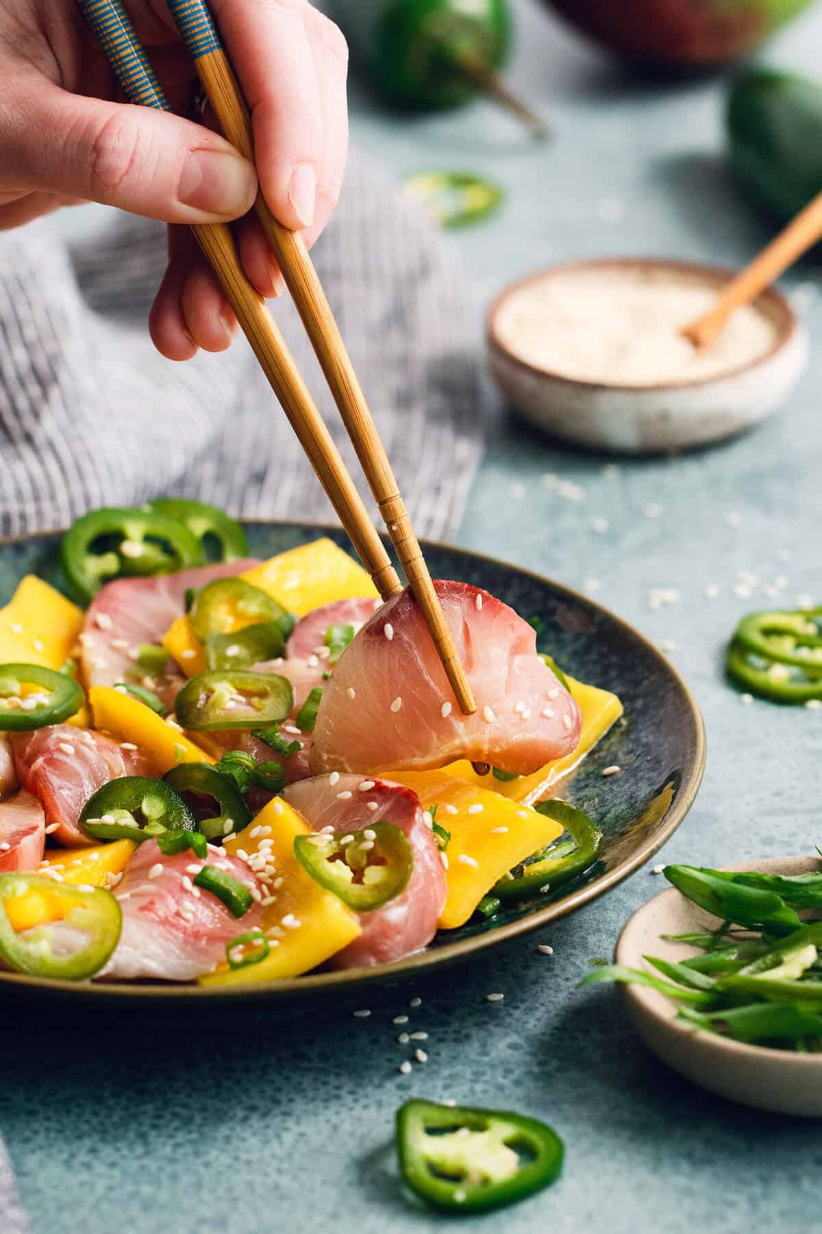Sweet mangoes and pickled jalapeño peppers make this Hamachi Crudo recipe a standout! It's an easy appetizer that always impresses. Chopsticks lifting hamachi crudo from plate