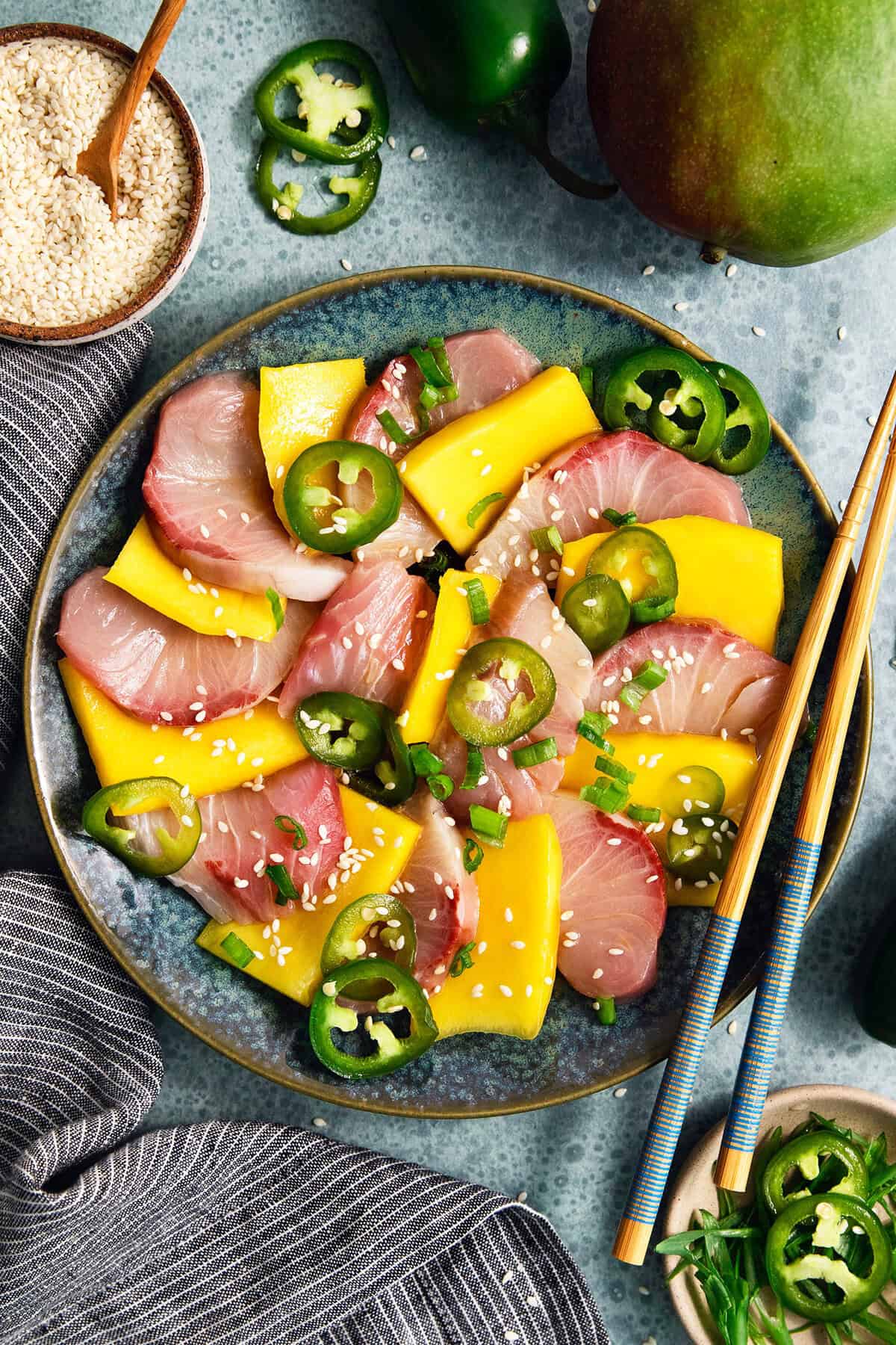 Sweet mangoes and pickled jalapeño peppers make this Hamachi Crudo recipe a standout! It's an easy appetizer that always impresses. Overhead view of hamachi crudo on plate with mango and pickled jalapenos