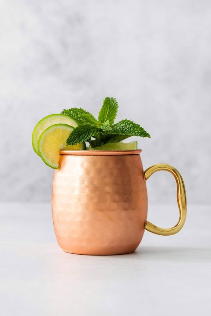 a Moscow mule cocktail in a copper mug with fresh lime and mint garnishes
