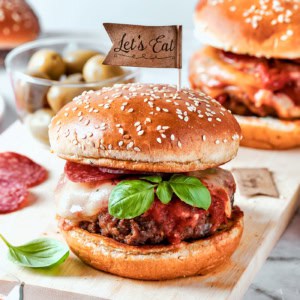 Pizza burgers are served on plates and garnished with basil leaves.