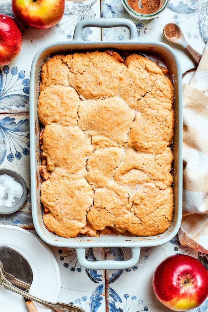Apple Cobbler has apple pie flavor in an easier form, swapping the crust for a biscuit-like topping that bakes up tender and golden brown! overhead photo of a white rectangular baking dish with baked Apple Cobbler