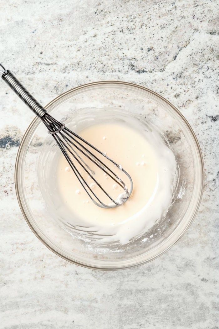Glaze for apple fritter bread in glass bowl with whisk.