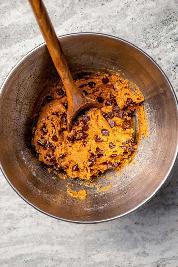 Soft, moist, and chewy, these Pumpkin Chocolate Chip Cookies are the perfect sweet treat for fall! Pumpkin pie spice adds warm, cozy flavor. Pumpkin chocolate chip cookie dough in bowl with wooden spoon.