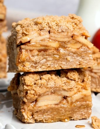 two apple pie bars stacked on top of each other, on a white plate