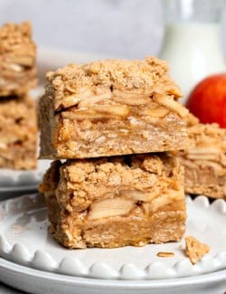 two apple pie bars stacked on top of each other, on a white plate