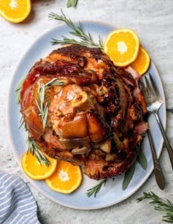 Glazed crockpot ham on platter with orange slices and rosemary.