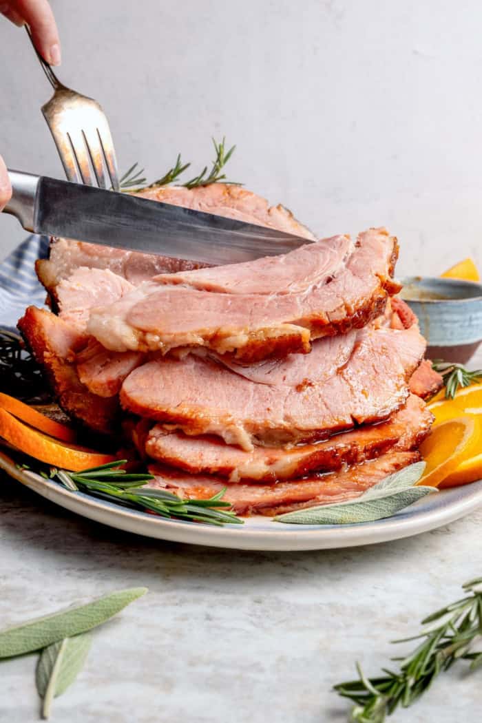 You just need two ingredients for the perfect juicy Crockpot Ham for a crowd! Add the optional glaze and gravy to take it to the next level. Fork and knife slicing into crockpot ham.