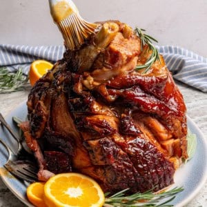 brushing a glaze over a cooked ham on a blue serving platter