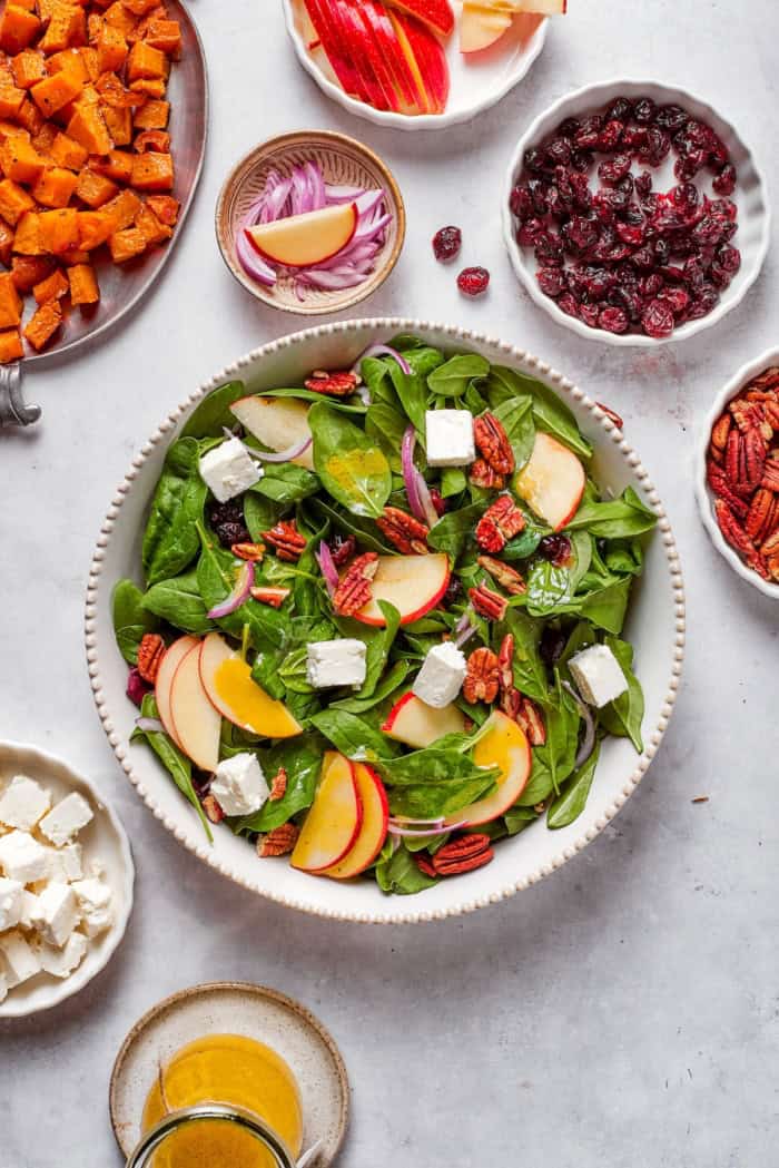 assembling a fall harvest salad in a white bowl