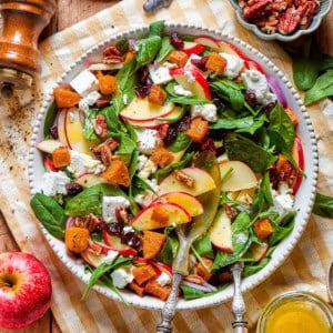 overhead photo of a wood table with a platter full of fall harvest salad with fresh greens, butternut squash, fresh greens, pecans, cranberries, and goat cheesegreens, pecans, cranberries, and goat cheese