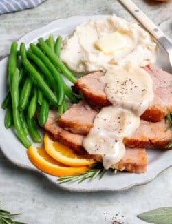 a plate of green beans, mashed potatoes, and sliced ham with ham gravy