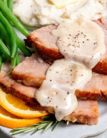 a plate of green beans, mashed potatoes, and sliced ham with ham gravy