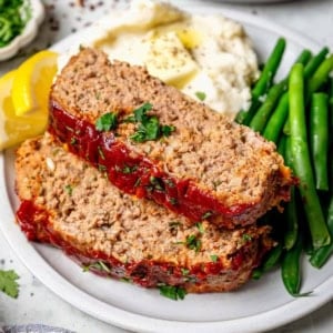 two slices of spicy meatloaf on a plate with mashed potatoes and green beans