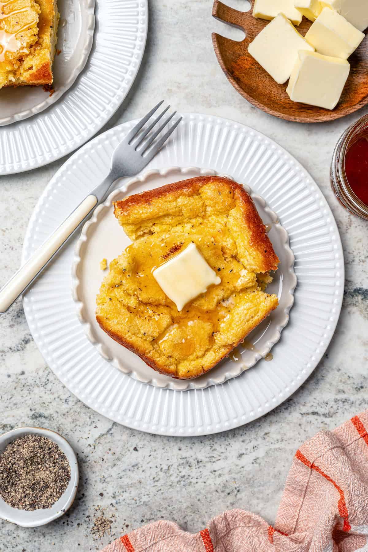 This Southern Spoon Bread recipe is fluffy, soft and lightly sweet, like a cross between cornbread and soufflé. A perfect holiday side dish! Spoon bread on plate with honey and butter.