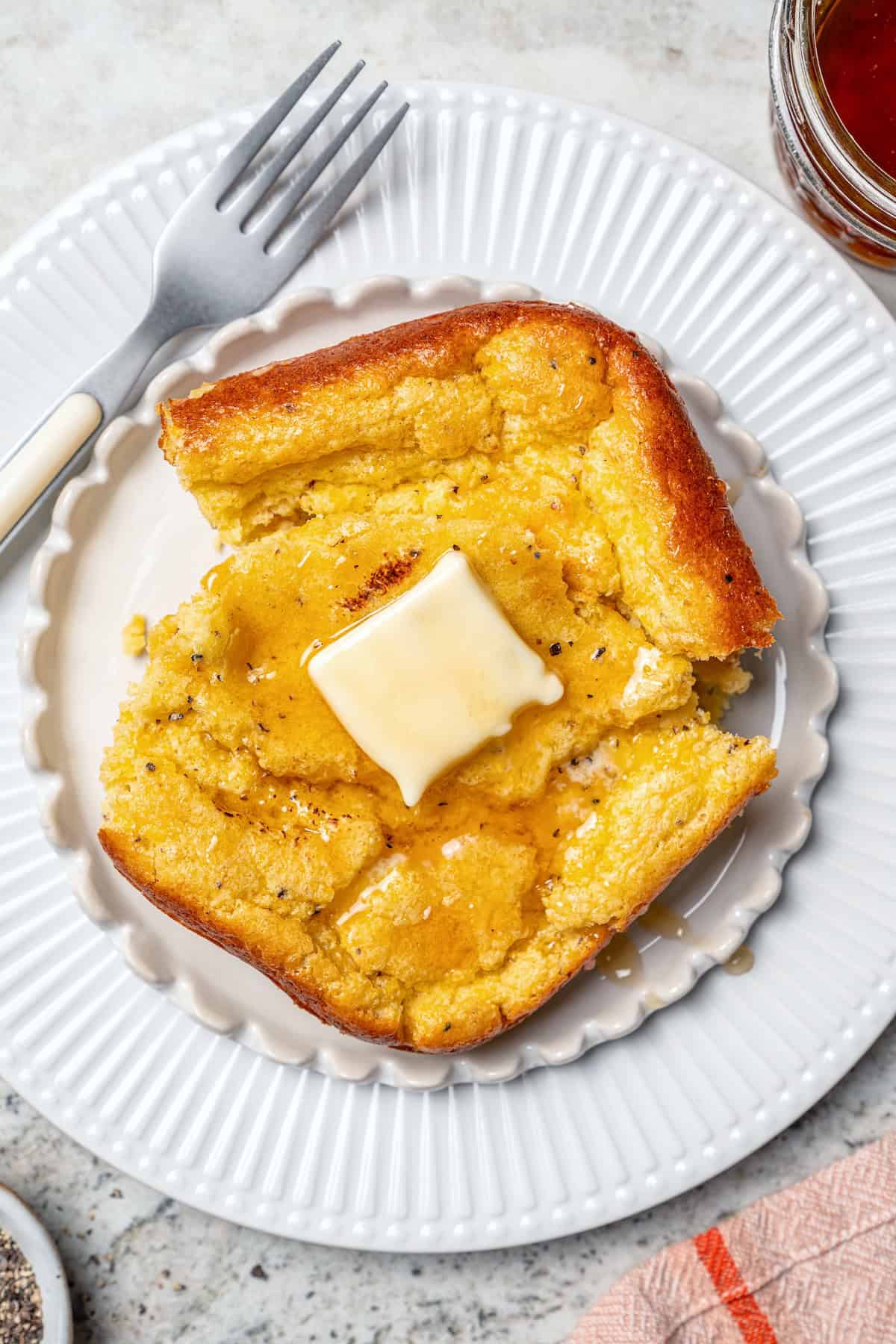 This Southern Spoon Bread recipe is fluffy, soft and lightly sweet, like a cross between cornbread and soufflé. A perfect holiday side dish! Plate with portion of spoon bread topped with honey and butter.