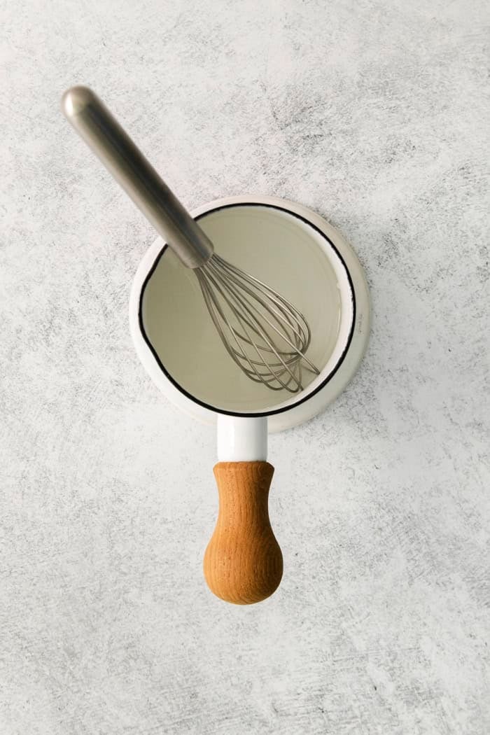 a whisk in a small white pan of simple syrup
