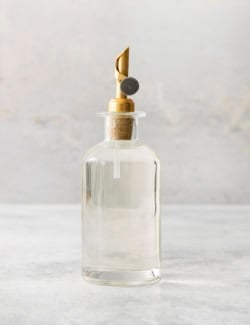 a clear bottle with a gold pour spout, full of simple syrup