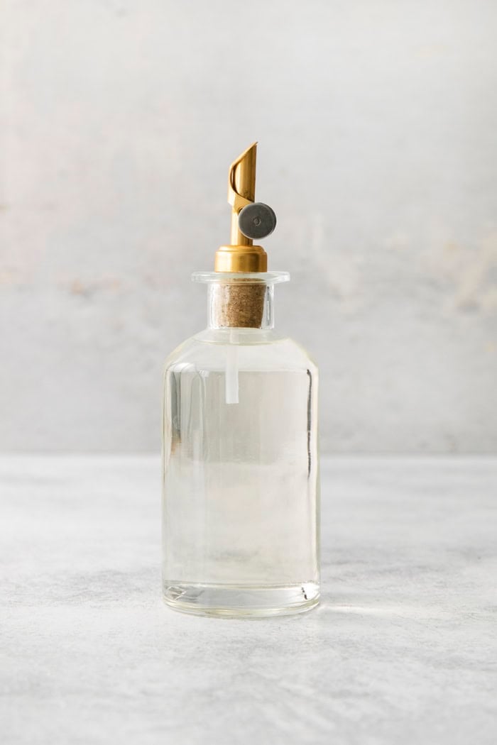 a clear bottle with a gold pour spout, full of simple syrup